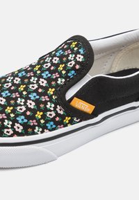 Chausson en toile noir avec un motif floral multicolore, semelle en caoutchouc blanche et étiquette logo Vans orange sur le côté.