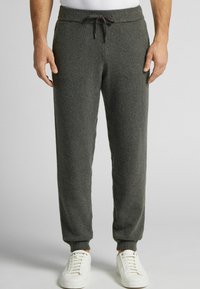 Šedé sametové joggingové kalhoty s elastickým pasem a šňůrkou. Hladké manžety a boční kapsy zvyšují funkčnost. V páru s bílými teniskami.