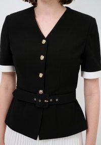 Schwarze taillierte Bluse mit kurzen Ärmeln und weißen Manschetten, mit goldenen dekorativen Knöpfen und einem passenden Gürtel in der Taille.