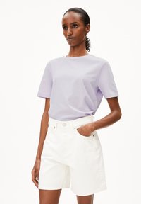 Hellblaues T-Shirt mit kurzen Ärmeln und rundem Halsausschnitt, kombiniert mit weißen Jeansshorts mit sichtbarem Taschen- und Knopfverschluss.