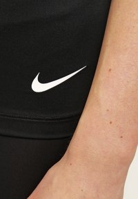 Leggings atléticos negros con un logo de Nike en forma de swoosh blanco en el costado, que presentan una tela suave y elástica y un diseño ajustado.