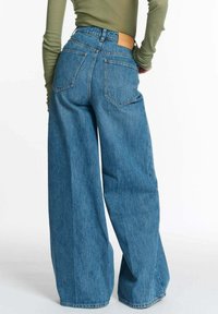 Wijde blauwe denim jeans met een hoge taille, voorzien van een leren label aan de achterkant en een klassiek achterzakontwerp. Textuurstof.