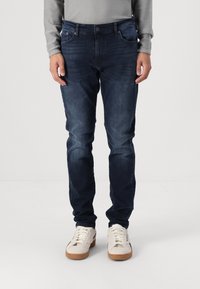 Mörkblå jeans med rak passform, denimmaterial, femficksdesign och subtil blekning. I kombination med ljusa sneakers.