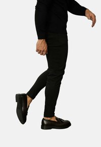 Pantalons slim noirs avec une texture lisse et un design fuselé, associés à des chaussures noires brillantes avec une plateforme basse et des détails en lacets.