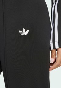 Black athletic pants with a small white Adidas logo on the thigh, featuring black and white striped accents on the side.