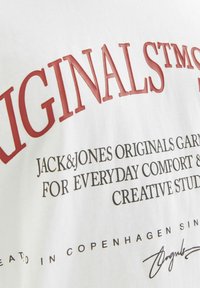 Hvid bomulds-t-shirt med iøjnefaldende rød og sort tekst, der står "ORIGINALS" samt andre brandingdetaljer, med en glat tekstur.