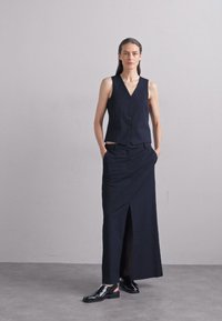 Navy blue sleeveless vest with buttons, paired with a long skirt featuring a front slit. Glossy black shoes complete the outfit.