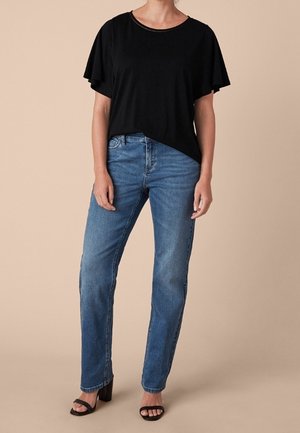 Top negro de manga corta con cuello redondo, combinado con jeans rectos de color azul claro. La modelo lleva sandalias de tacón negro.