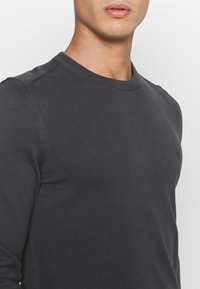 Dunkelgrauer gerippter Pullover mit Rundhalsausschnitt, der ein dezentes Logo-Detail auf der Brust und eine taillierte Silhouette aufweist.