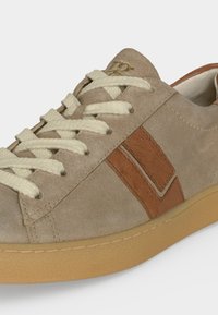 Baskets en daim marron clair avec lacets crème, bandes en cuir marron foncé sur les côtés et semelle en caoutchouc gomme sur fond blanc.