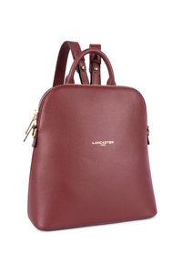 Zaino in pelle borgogna con accenti dorati, forma arrotondata, chiusura con zip e manici superiori doppi, caratterizzato da una superficie testurizzata e logo del marchio.