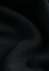 Tessuto nero a maglia che mostra una superficie morbida e testurizzata con un delicato motivo a coste, drappeggiato in pieghe fluide.