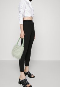 Pantaloni neri attillati con una texture liscia, abbinati a sandali neri con tacco alto e apertura sulle dita, caratterizzati da un accento metallico. In mano una borsa fluffy di colore verde menta.