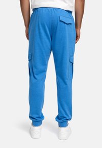 Blaue Baumwoll-Cargo-Hose mit entspanntem Schnitt, ausgestattet mit Seitentaschen und hinteren Klappen-Taschen. Kombiniert mit weißen Sneakern für einen Kontrast.