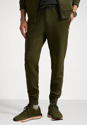 Olive green sweatpants made of soft fabric, featuring a drawstring waist, tapered leg design, and contrasting stitching details, paired with matching sneakers.
