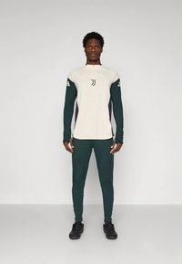 Langærmet atletisk top i off-white med mørkegrønne detaljer og en kvart lynlås, kombineret med matchende tætsiddende bukser.