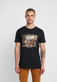 Sort bomulds t-shirt med et farverigt, vintage-inspireret print af en gruppe scene med teksten "In Da Club" under billedet.