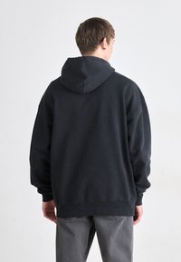 Felpa nera con cappuccio realizzata in tessuto morbido, caratterizzata da un cappuccio ampio, vestibilità comoda e polsini a coste. Il retro presenta un design minimalista senza grafiche.