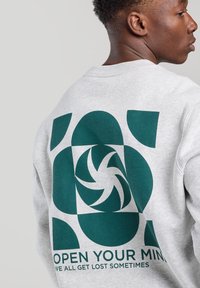Gray sweatshirt with a large green graphic design on the back featuring swirls and shapes, accompanied by text reading “OPEN YOUR MIND.”