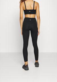 Černý sportovní croptop a legíny s vysokým pasem vyrobené z elastického materiálu, s logem na topu a hladkým povrchem po celé délce.