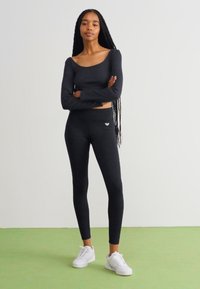 Black long-sleeve top and leggings made of stretch fabric; form-fitting design; paired with white sneakers; minimal branding detail.