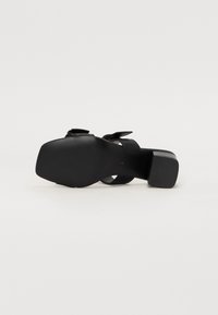 Svart högklackad sandal med kvadratisk tådesign, mjukt lädermaterial, justerbar ankelsnodd och texturerad gummisula för bra grepp.