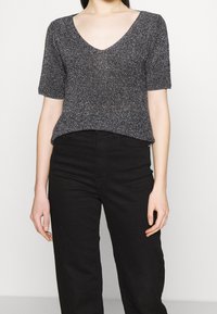 Top nero a maniche corte con scollo a V, realizzato in tessuto testurizzato con fili metallici. Abbinato a pantaloni neri a vita alta.