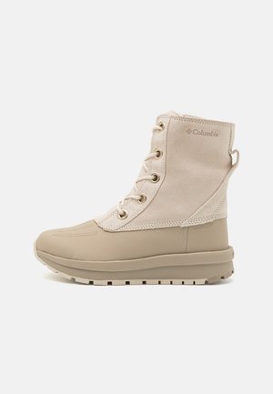 Beige vandtæt støvle lavet af ruskind og gummi, med snørebåndsdesign, teksturerede accenter og en polstret sål for komfort.