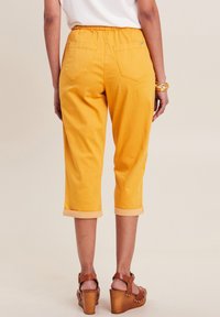 Gele cropped broeken hebben een elastische tailleband, twee achterkantzakken en opgerolde manchetten. Gecombineerd met bruine platform sandaal voor contrast.