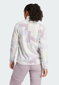 Sudadera de forro polar en crema con patrones geométricos abstractos en morado claro, cuello alto, mangas largas y silueta ajustada.