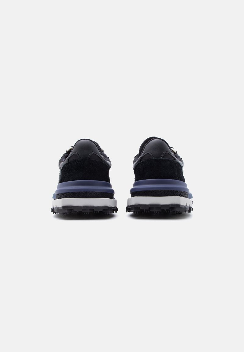 Coppia di sneakers nere e blu navy con suole testurizzate viste da dietro su sfondo grigio chiaro.