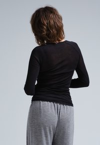Schwarzes Langarmoberteil mit einer figurbetonten Passform und Rippstruktur, kombiniert mit grauen Jogginghosen mit Kordelzug aus einem weichen, leichten Stoff.