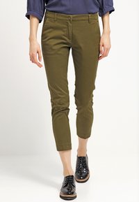 Olive green spodnie w kroju cropped, wykonane z bawełny elastycznej, z dopasowanym krojem, z przodem na guziki, kieszeniami bocznymi i podwiniętymi mankietami. Czarnym butom dopełnia stylizację.