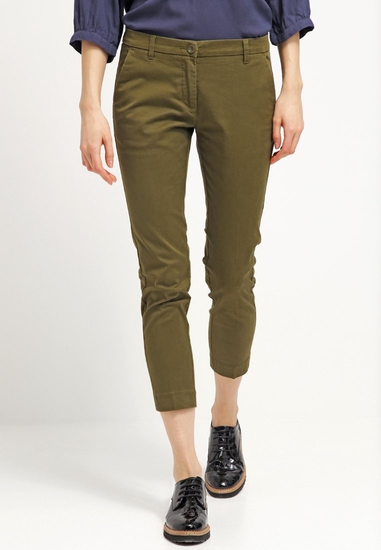 Olive green spodnie w kroju cropped, wykonane z bawełny elastycznej, z dopasowanym krojem, z przodem na guziki, kieszeniami bocznymi i podwiniętymi mankietami. Czarnym butom dopełnia stylizację.