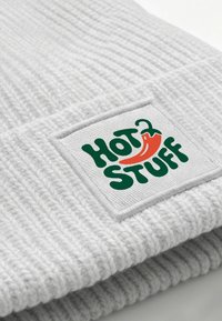 Gray knitted beanie with a ribbed texture, featuring a rectangular white patch with "HOT STUFF" text and a red chili pepper graphic.