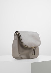 Borsa a mano in pelle grigia con finitura testurizzata, top a patta e dettaglio della zip dorata. Presenta una tasca laterale con zip e una silhouette arrotondata.