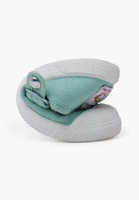 Zapatilla de lona verde con suela blanca de goma, que presenta una tapa con cierre a presión y una etiqueta colorida que representa un personaje.