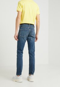 Blå denimjeans med slim fit, med två bakfickor, tillsammans med en kortärmad gul polotröja och ljusgrå sneakers.