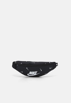 Sac banane noir Nike avec logos Swoosh blancs et compartiment principal zippé sur fond gris clair.