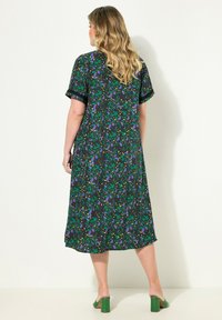 Robe florale en tissu noir avec un motif vert et violet, à manches courtes, de longueur genoux et à coupe décontractée. Chaussures à talons blocs vertes.