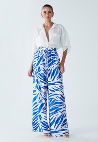 Chemise blanche à manches courtes avec deux poches, associée à un pantalon large fluide bleu et blanc à motifs avec une taille à cordon.
