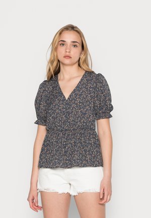 Blusa floral azul-marinho com decote em V, mangas bufantes e cintura elástica, combinada com calções brancos rasgados. Padrão floral em tons de rosa e creme.
