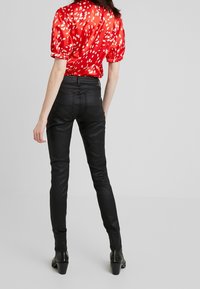 Blusa corta de satén roja de manga corta con puntos blancos, combinada con pantalones de cuero negro ajustados y botas de tobillo negras con tacón.