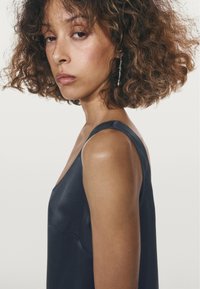 Satin donkerblauwe jurk met dunne banden, met een gladde textuur en een subtiele glans. Gebogen halslijn met een aansluitende silhouet.