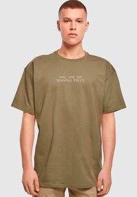 Olivengrøn oversized T-shirt med korte ærmer, prydet med præget tekst "DU ER MIT MANGLENDE STYKKE" foran.