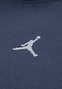 Mørkeblått stoff med en teksturert overflate som har en hvit brodert logo av en hoppende figur som holder en basketball.