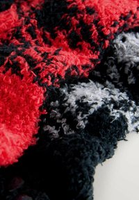 Karo-musterter Stoff in Rot, Schwarz und Grau. Faserige, weiche Textur mit einem geschlungenen Muster, das Tiefe und visuelles Interesse erzeugt.