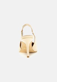 Escarpin beige à talon haut avec bout pointu, bride arrière et talon aiguille. Matériau en cuir lisse avec une finition légèrement brillante.