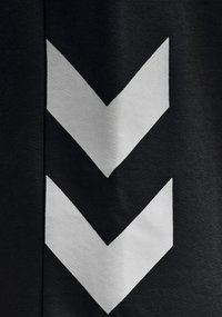 Dos grandes chevrones blancos apuntando hacia abajo sobre una tela negra texturizada, probablemente parte de una prenda o un diseño textil.