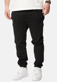 Black sweatpants made of soft fabric, tapered fit with cuffed ankles. Worn with white sneakers, featuring a simple design without patterns.